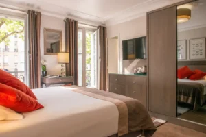 Valoisa hotellihuone, jossa on parveke ja näkymä Pariisin kadulle.